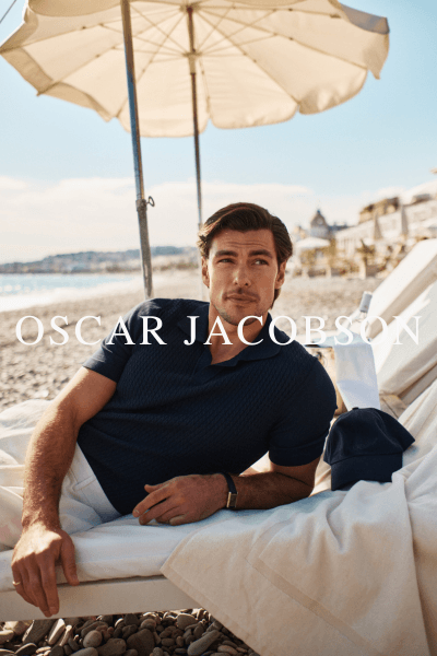 Modell lener seg på en solseng på en strand iført klær fra Oscar Jacobson